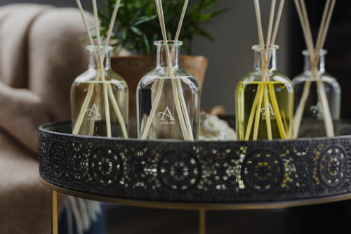 4 Reed Diffusers on a side table, varying colours from clear to yellow/gold